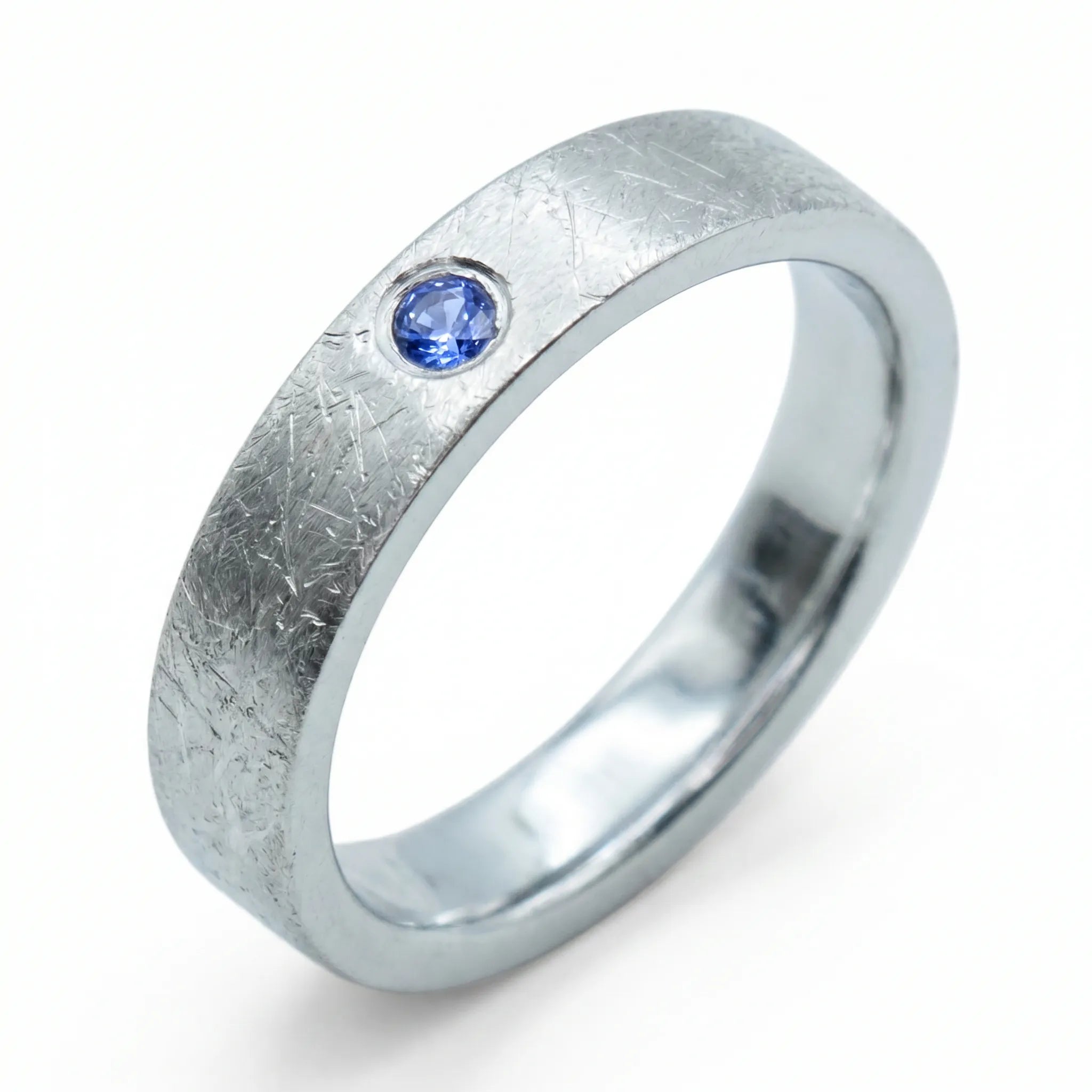 Close-up of sterling silver ring with blue topaz flush set stone and textured surface