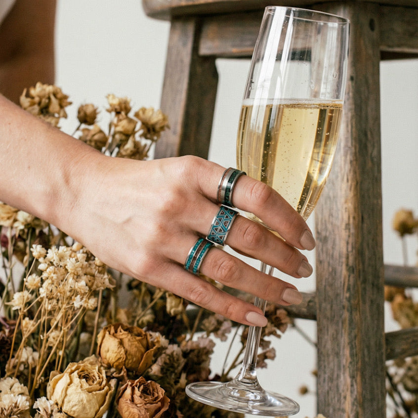Hand holding a champagne glass wearing three best selling modern rings from Venus Rings collection