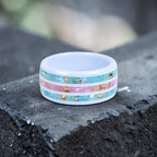 Bloomstripe white ceramic ring featuring three floral inlay channels with real flower petals, iridescent accents, and gold leaf details.