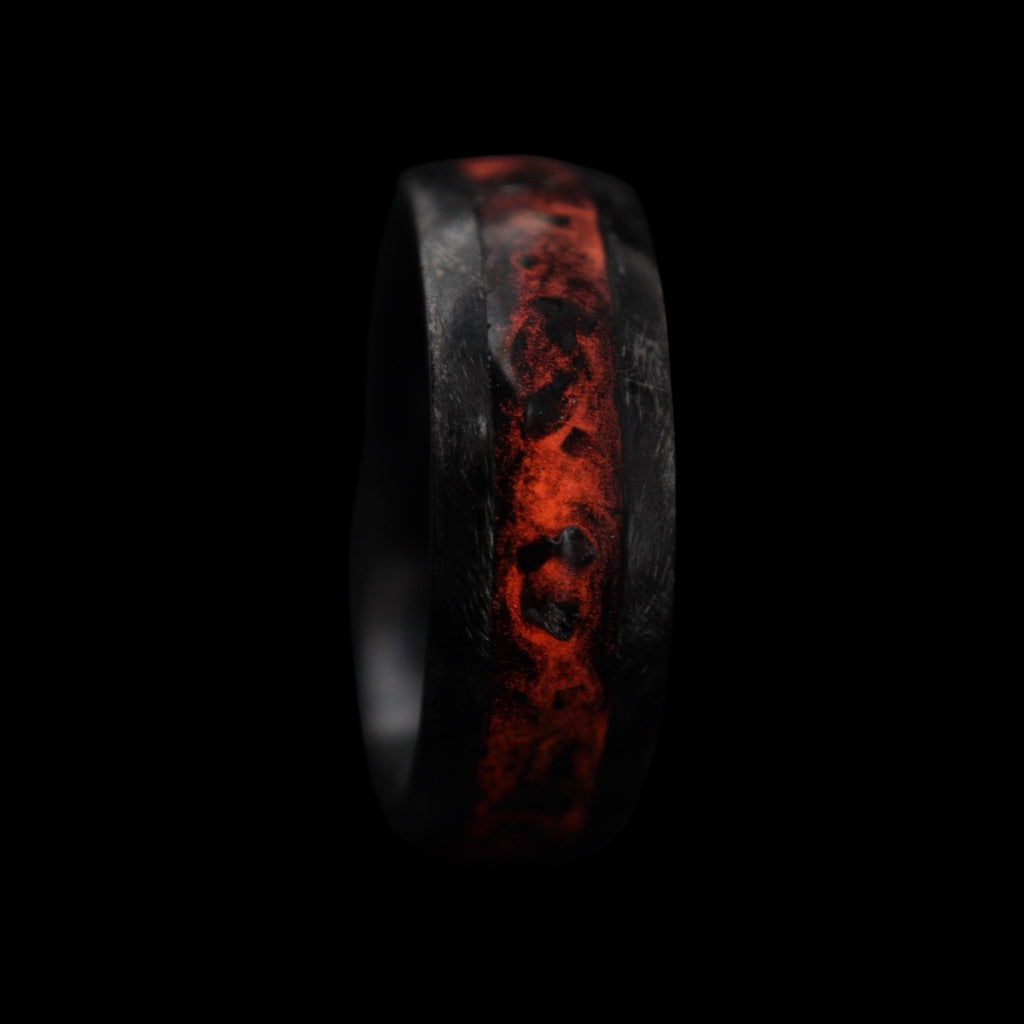 Cataclysm black titanium ring featuring meteorite fragments, blue dinosaur bone, lava stone inlay, and red glow accents with a rugged distressed finish.