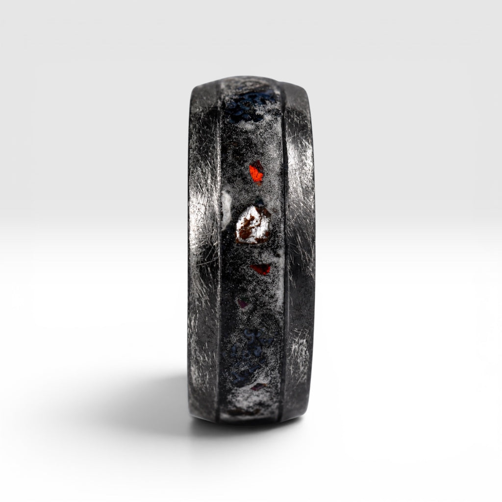 Cataclysm black titanium ring featuring meteorite fragments, blue dinosaur bone, lava stone inlay, and red glow accents with a rugged distressed finish.