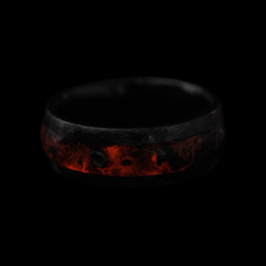 Cataclysm black titanium ring featuring meteorite fragments, blue dinosaur bone, lava stone inlay, and red glow accents with a rugged distressed finish.