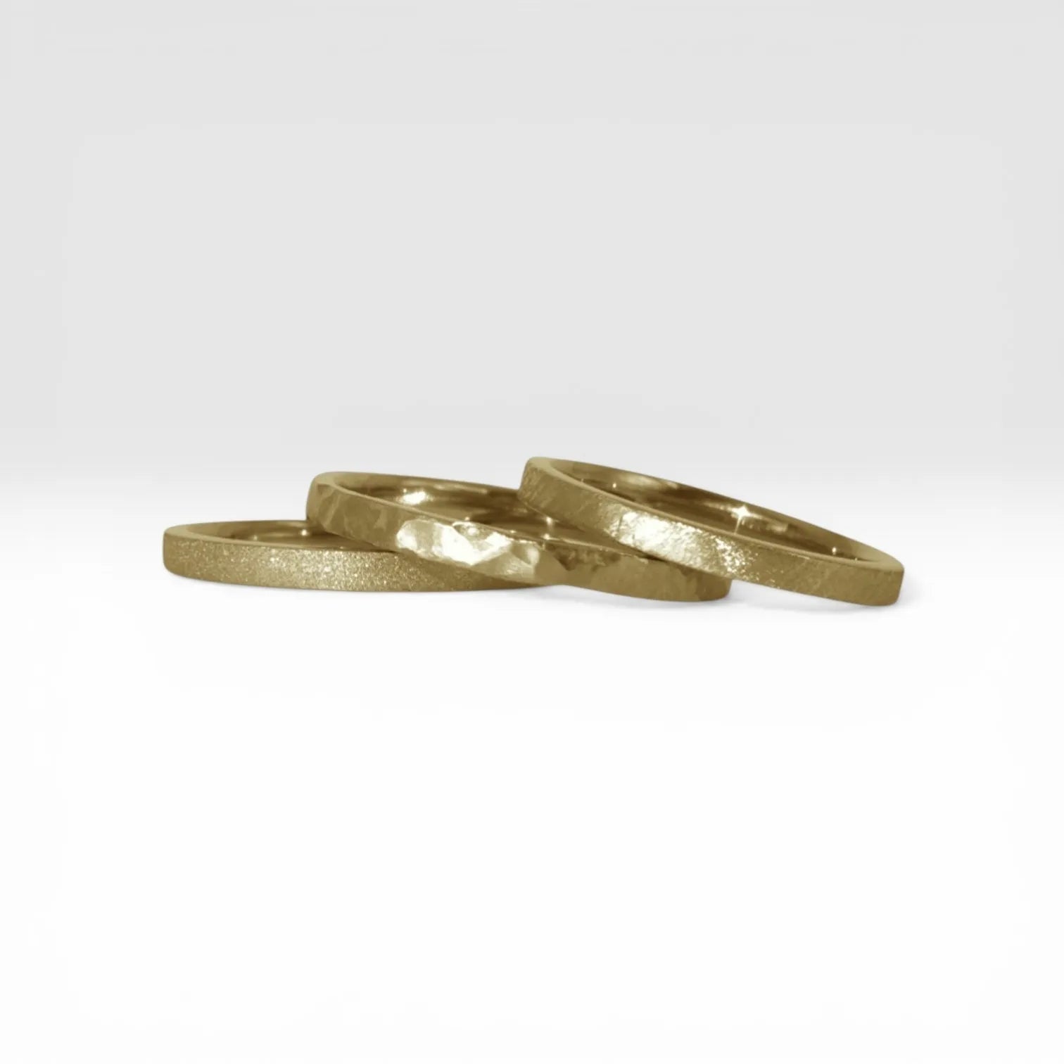 Órbita stack set — three gold stacking rings with different handcrafted finishes laid out for mix and match styling