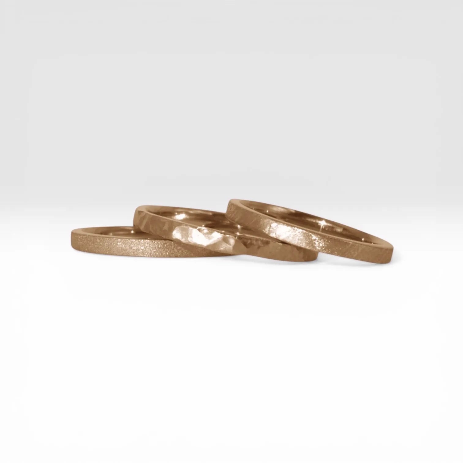 Órbita stack set — three rose gold stacking rings with different handcrafted finishes laid out for mix and match styling
