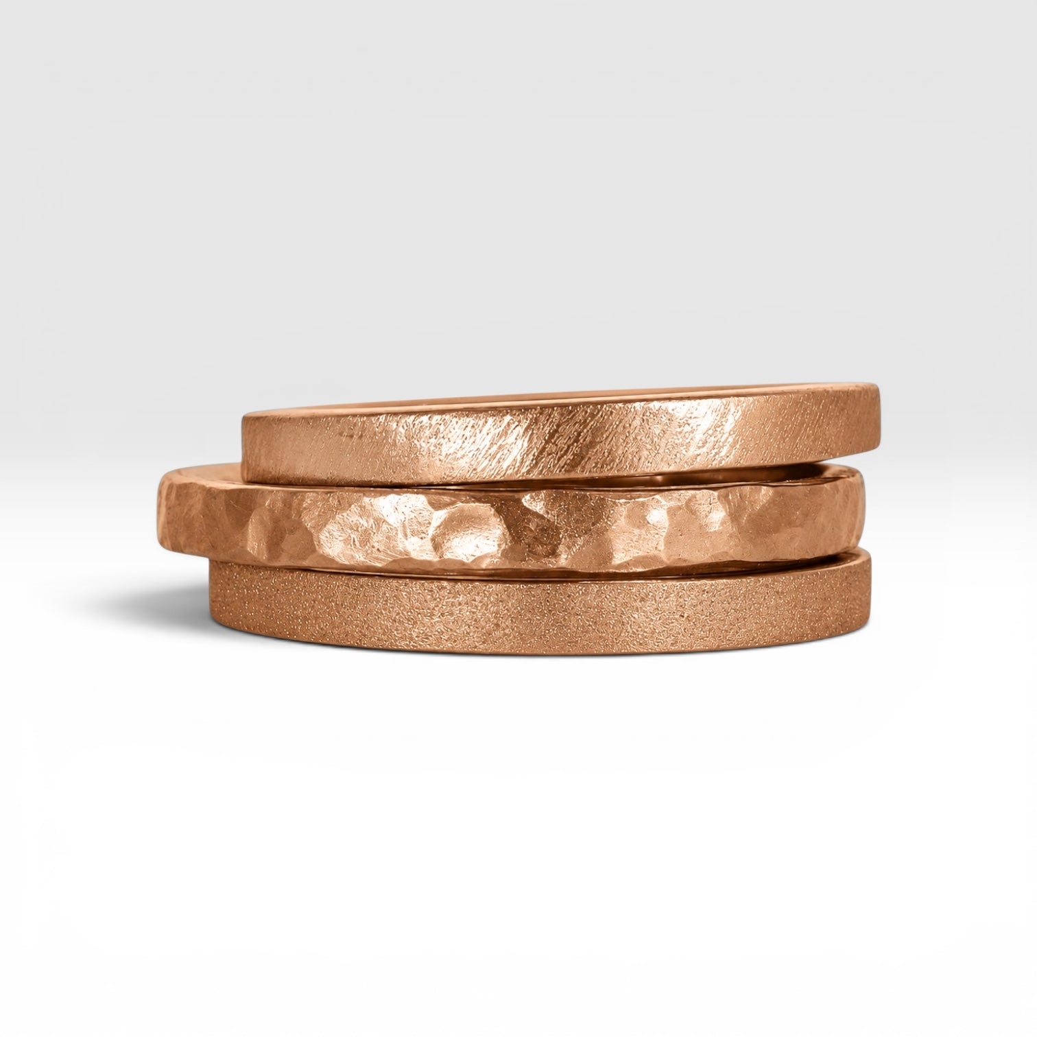 Órbita collection — three 2mm rose gold stackable rings stacked together showing hammered, frosted, and diagonal textures, handcrafted in Utah