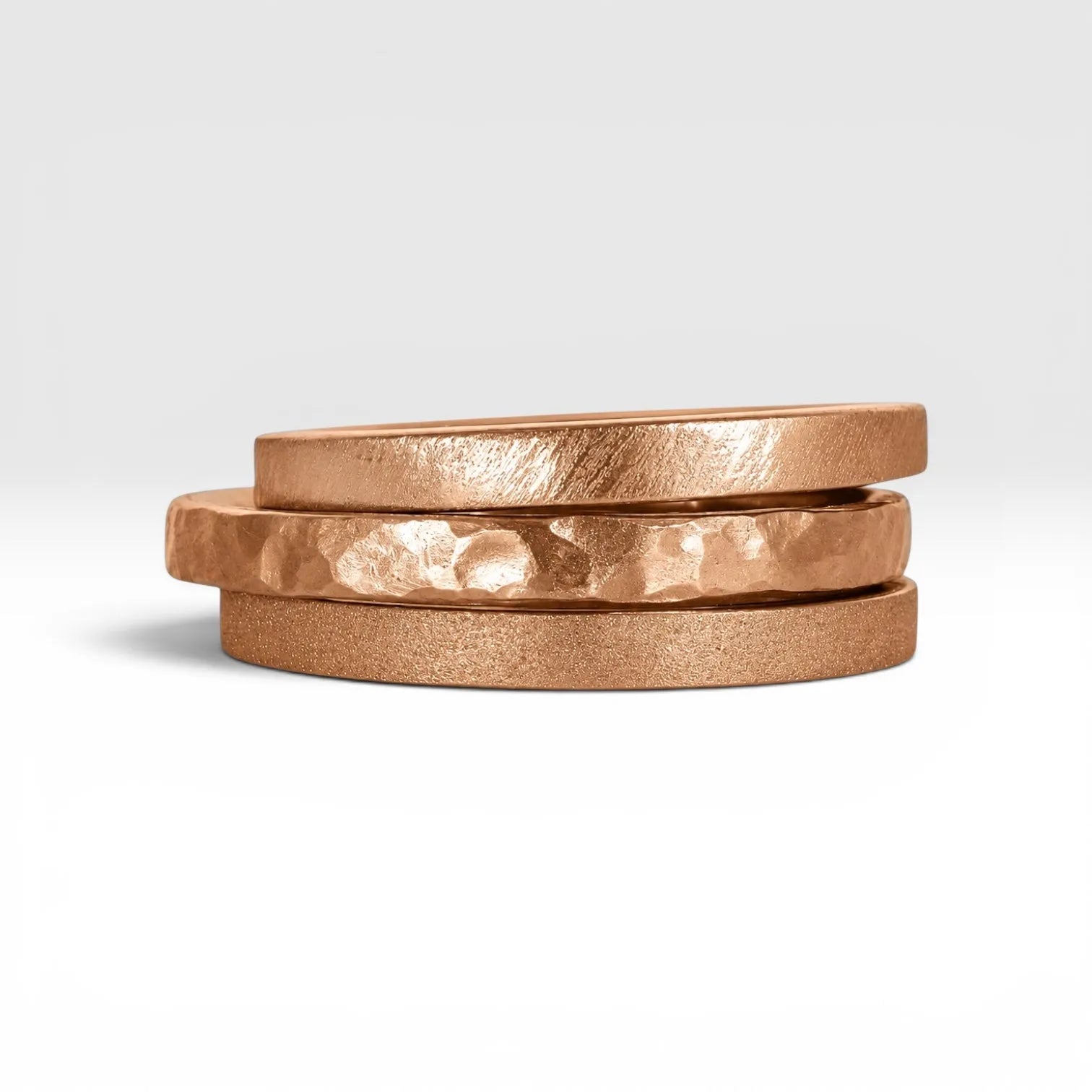 Órbita collection — three 2mm rose gold stackable rings stacked together showing hammered, frosted, and diagonal textures, handcrafted in Utah
