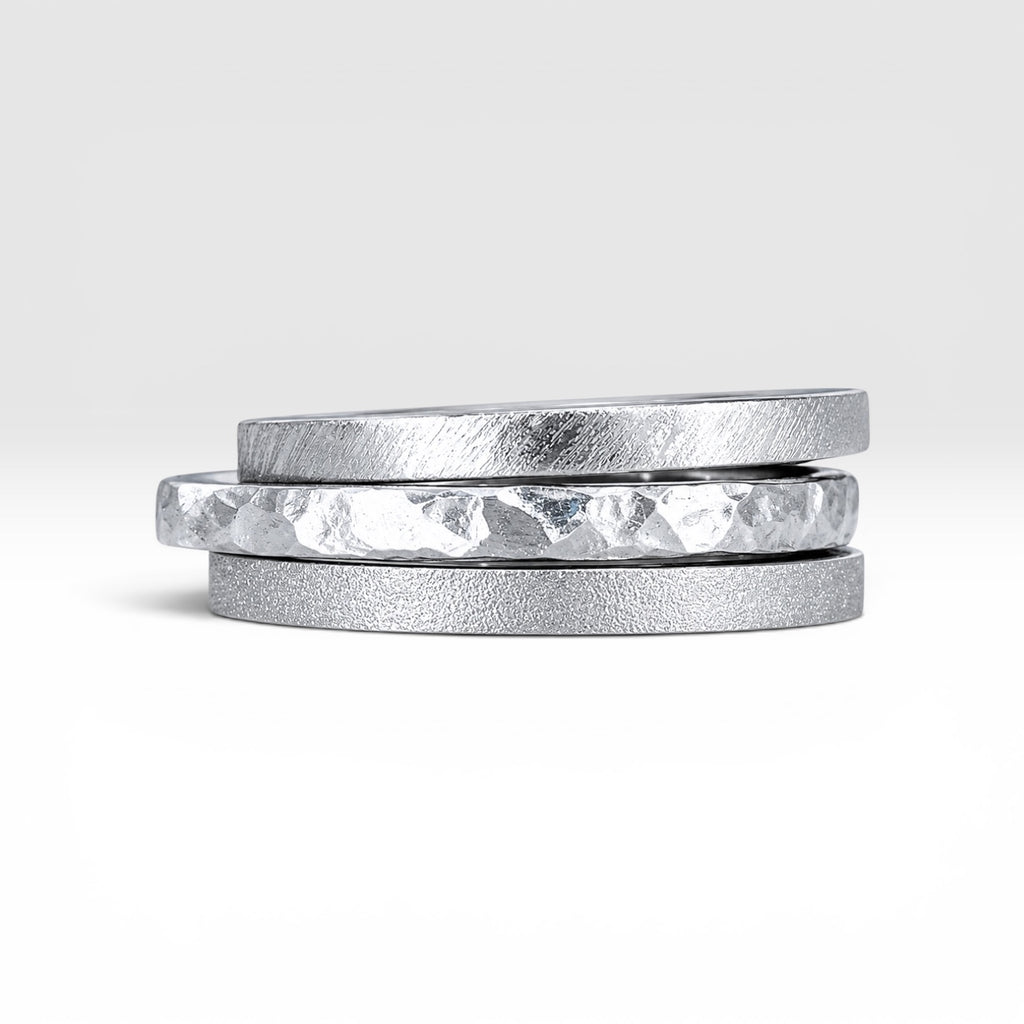 Órbita collection — three 2mm sterling silver stackable rings stacked together showing hammered, frosted, and diagonal textures, handcrafted in Utah