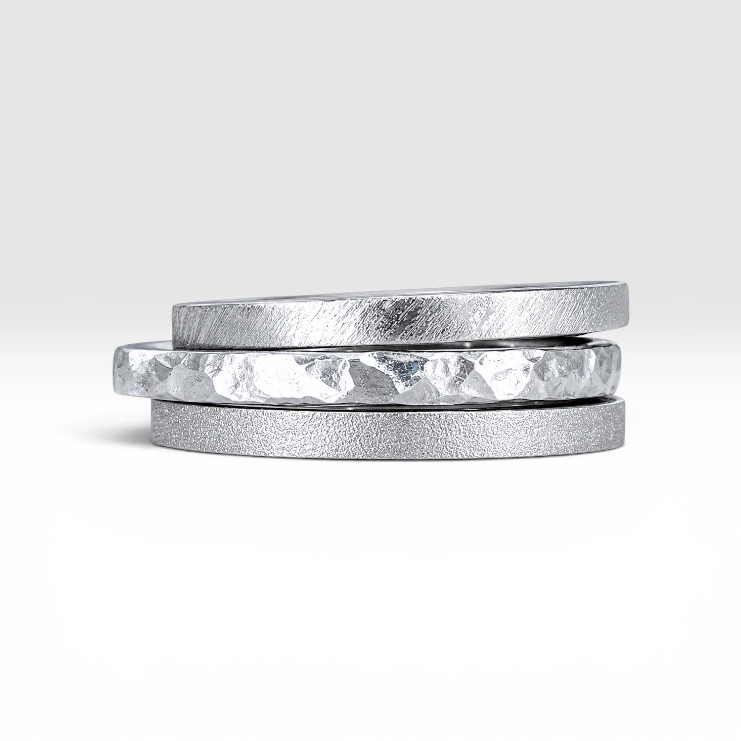 Órbita collection — three 2mm sterling silver stackable rings stacked together showing hammered, frosted, and diagonal textures, handcrafted in Utah