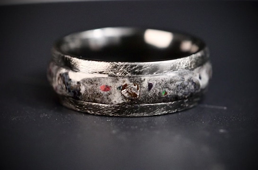 Cataclysm black titanium ring featuring meteorite fragments, blue dinosaur bone, lava stone inlay, and red glow accents with a rugged distressed finish.