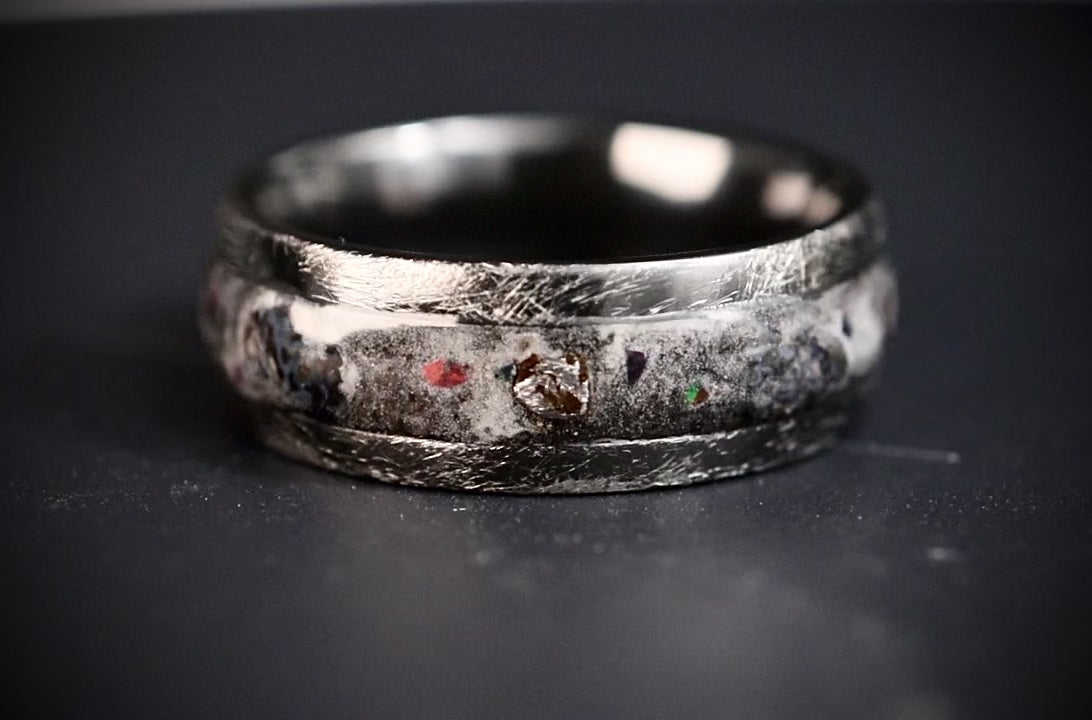 Cataclysm black titanium ring featuring meteorite fragments, blue dinosaur bone, lava stone inlay, and red glow accents with a rugged distressed finish.