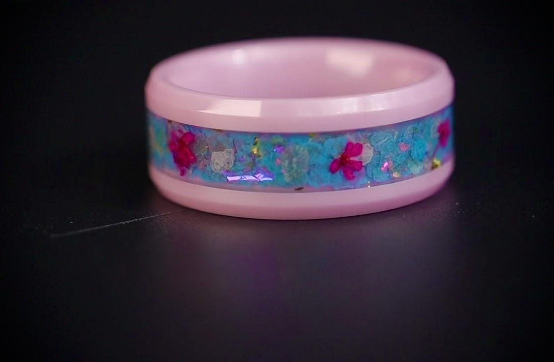 Skyblossom pink ceramic ring featuring preserved blue flower petals, pink pressed flowers, and iridescent accents in a handcrafted floral inlay.
