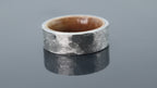 Forged texture tungsten ring with warm wood sleeve interior creating a rugged contrast