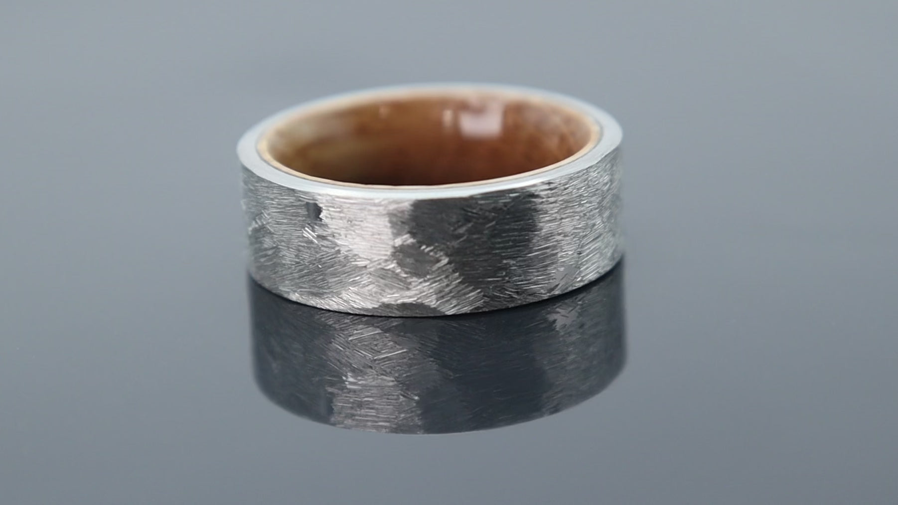 Forged texture tungsten ring with warm wood sleeve interior creating a rugged contrast