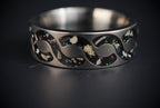 Abyssforge titanium ring featuring Megalodon tooth fragments, Campo del Cielo meteorite shavings, Mount Etna lava stone, green opal accents, and a sculpted flowing pattern.