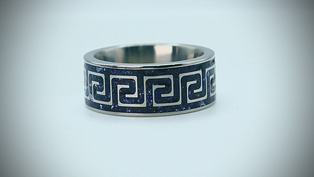 Titanium ring with Greek key pattern inlaid with blue goldstone and silver leaf creating a galaxy-like effect.