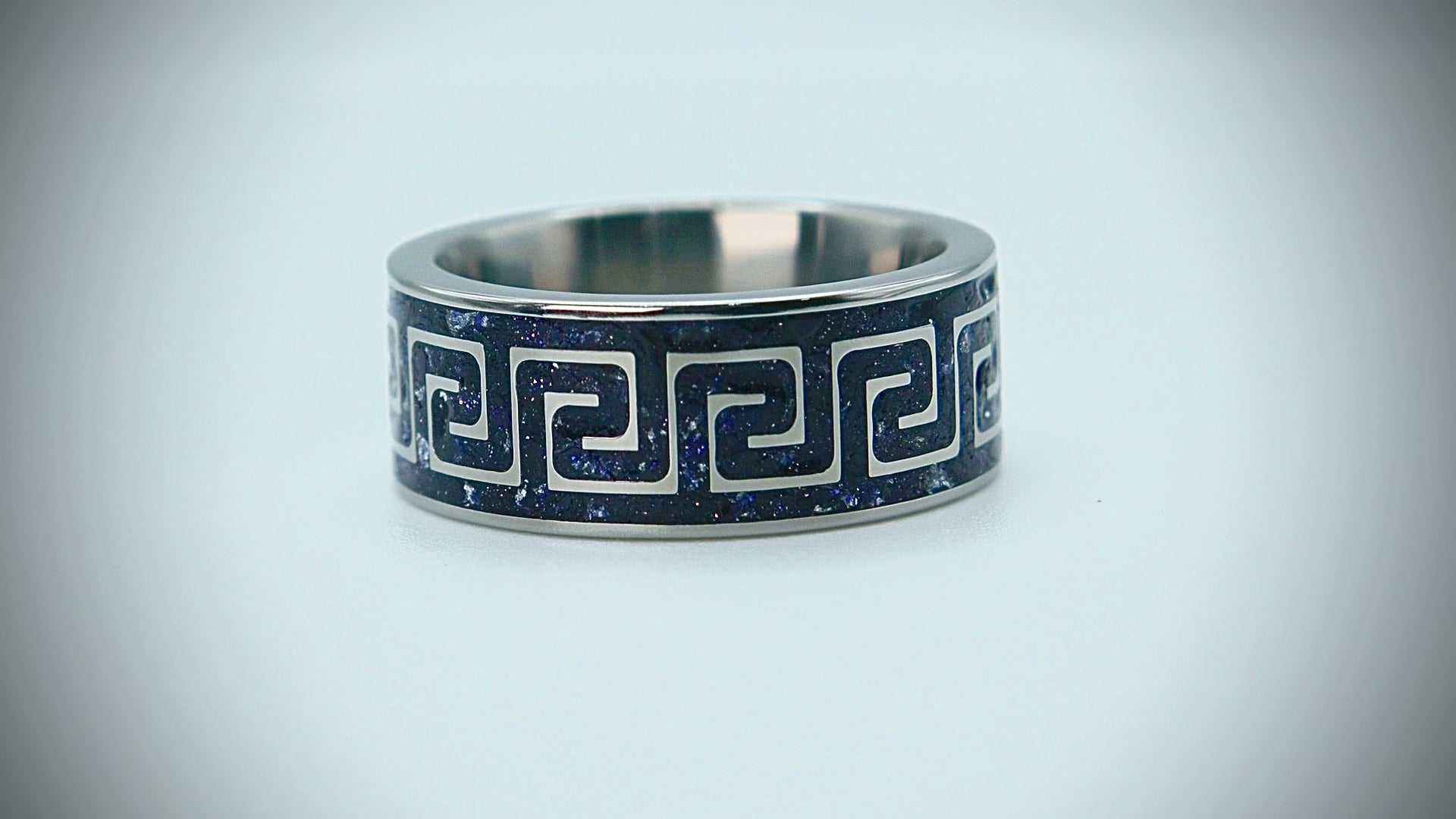 Titanium ring with Greek key pattern inlaid with blue goldstone and silver leaf creating a galaxy-like effect.