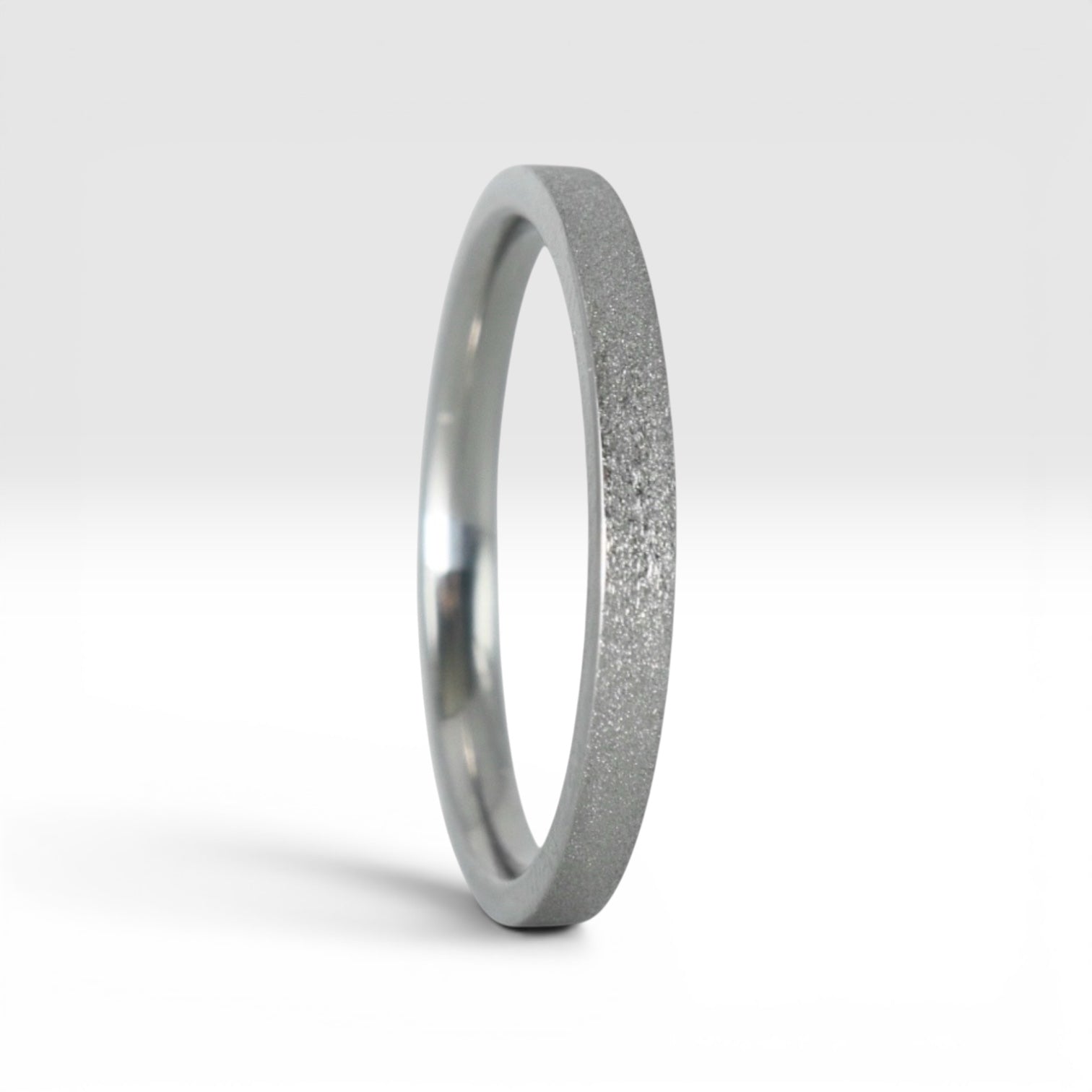 Upright view of órbita luz frosted titanium stacking ring showing fine sparkle texture and polished interior